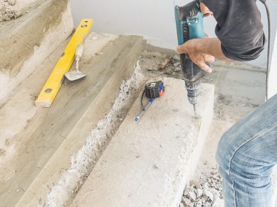 Partial focus of a man is working with reinforce concrete stair structure modification using hand drill machine in construction site